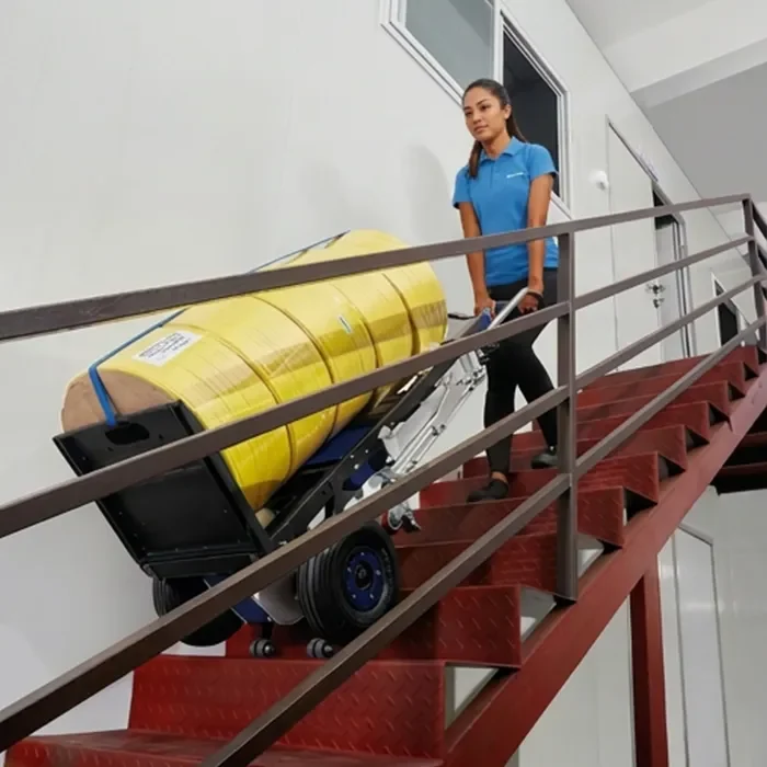 Mujer operando un sube escaleras eléctrico para mover mercancía voluminosa sin esfuerzo físico, garantizando salud laboral y prevención de riesgos.